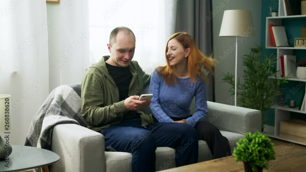 A young couple watching a fun video on a smartphone in their cozy living room A young couple watching a fun video on a smartphone in their cozy living room