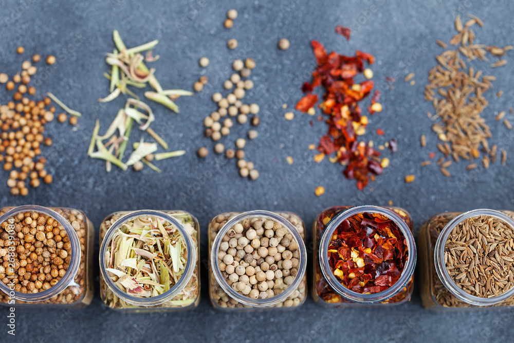 Assortments of spices in jars on grey stone background. Top view. Copy space.