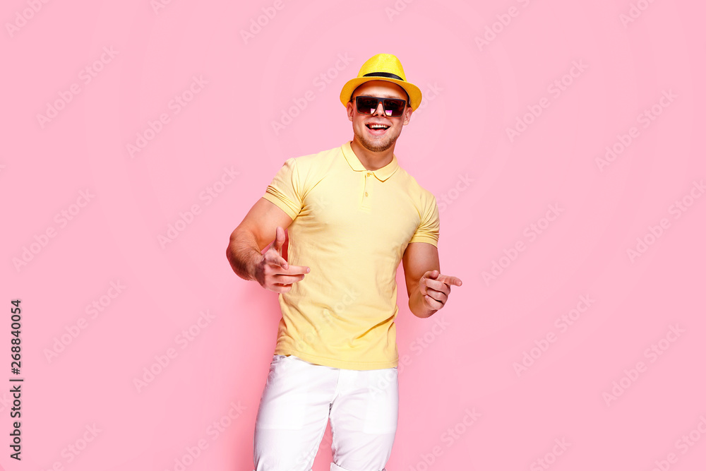 Positive young male in trendy outfit smiling and pointing at camera while standing against pink background