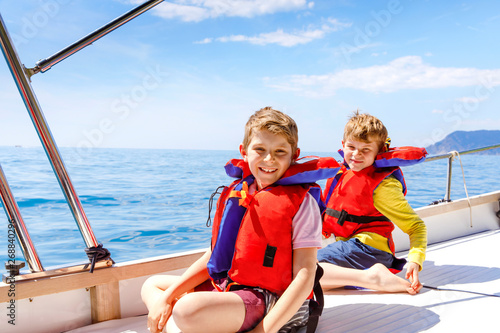 Two little kid boys, best friends enjoying sailing boat trip. Family vacations on ocean or sea on sunny day. Children smiling. Brothers, schoolchilden, siblings having fun on yacht.