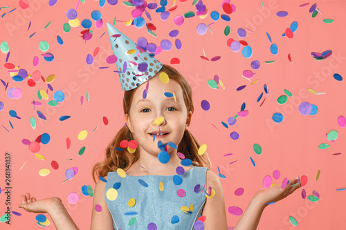 Cheerful little girl celebrates birthday. A child is standing in a rain of confetti. A party. Closeup portrait on pink background.