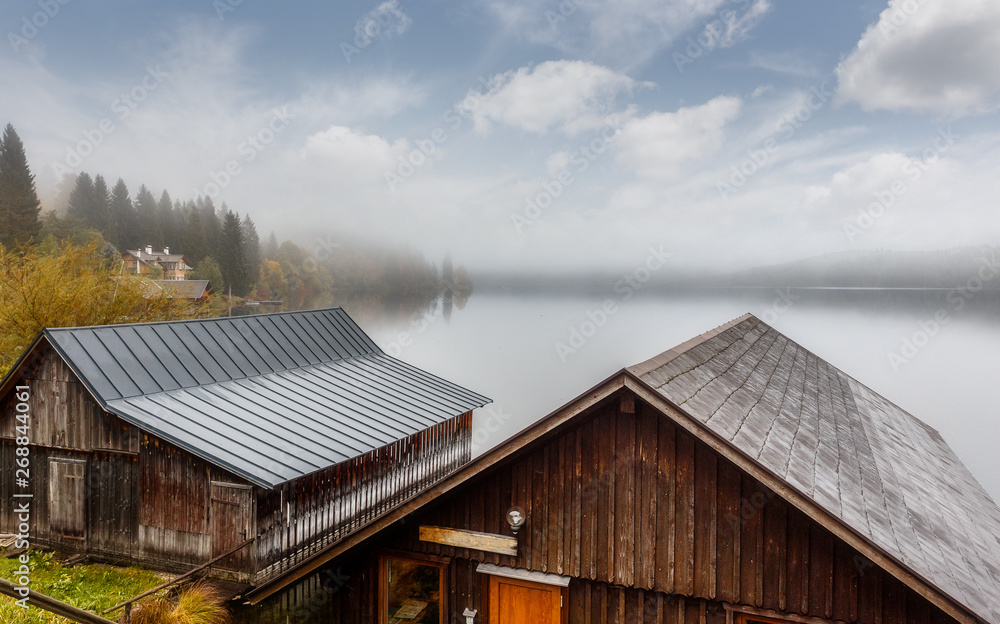 Magic Morning on Altausser lake. Wooden Fishing Huts on the shore of the Alpine lake. The sky is shining through the morning fog. Dramatic unusual scene. Awesome Austrian landscape. nature background