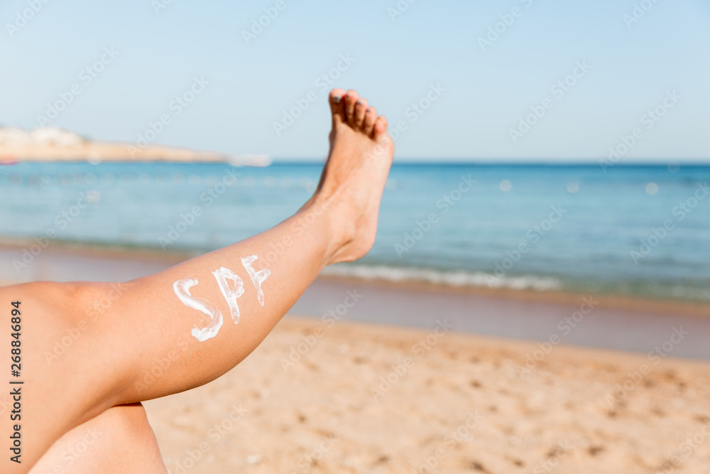 Raised up female leg with spf word made of sun cream at the beach. Sun protection factor concept Raised up female leg with spf word made of sun cream at the beach. Sun protection factor concept