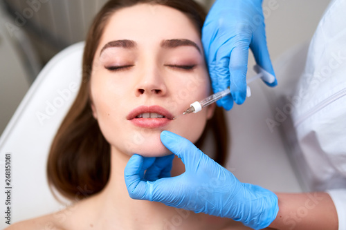 Lip Augmentation. Closeup Of Beautician Doctor Hands Doing Beauty Procedure To Female Lips with Syringe. Young Woman s Mouth Receiving Hyaluronic Acid Injection. Cosmetology Treatment. Filler Therapy.