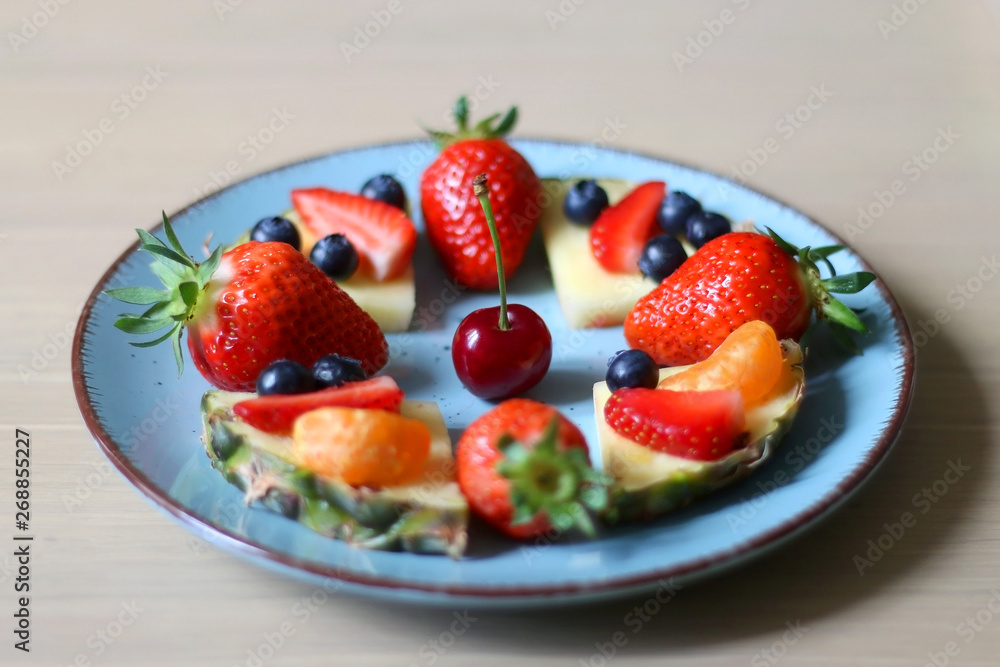 Various spring fruit on a turquoise plate: strawberries, pineapple, blueberries,tabgerine and cherry. Selective focus.