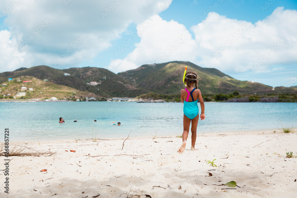 Little girl in vibrant coloured swimsuit and scuba goggles standing on a white sandy beach and looking out to the sea. Little girl in vibrant coloured swimsuit and scuba goggles standing on a white sandy beach and looking out to the sea.