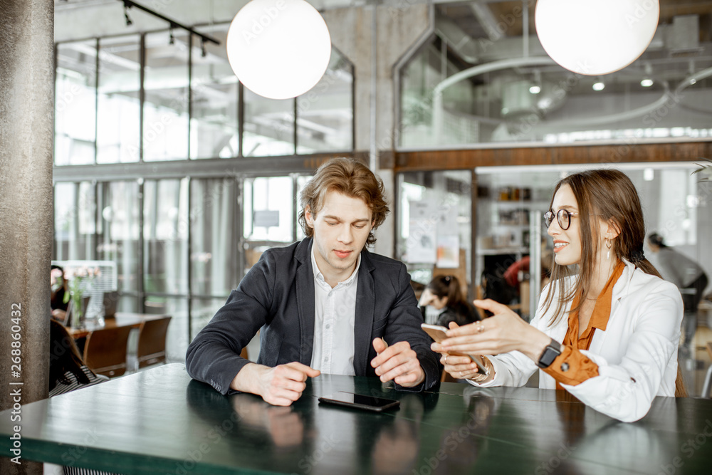 Young man and woman having business conversation while sitting together in the bar or coworking space
