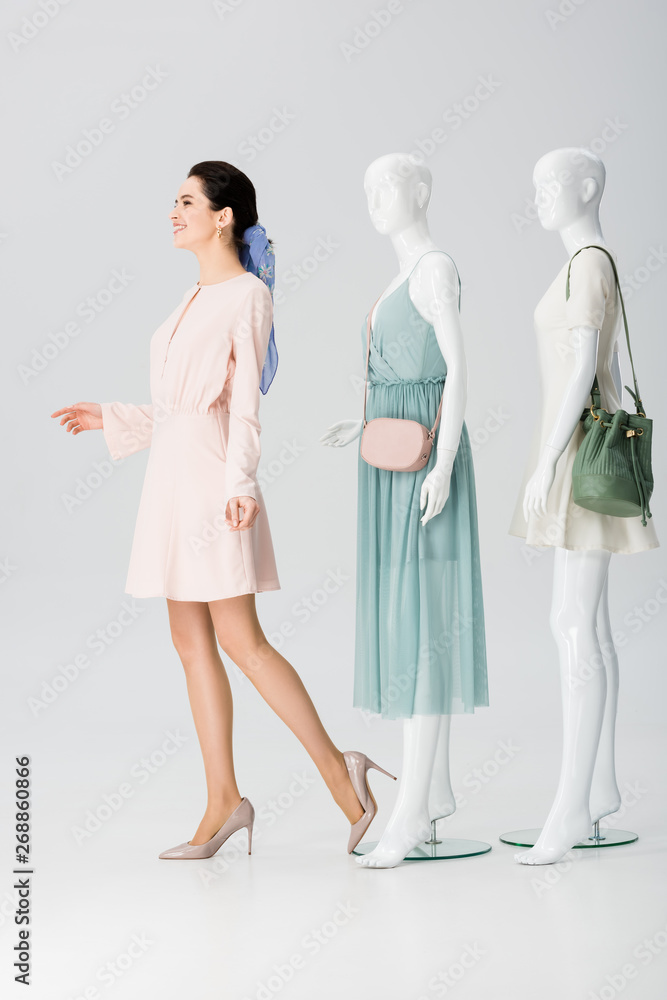 beautiful smiling girl posing with mannequins in dresses on grey