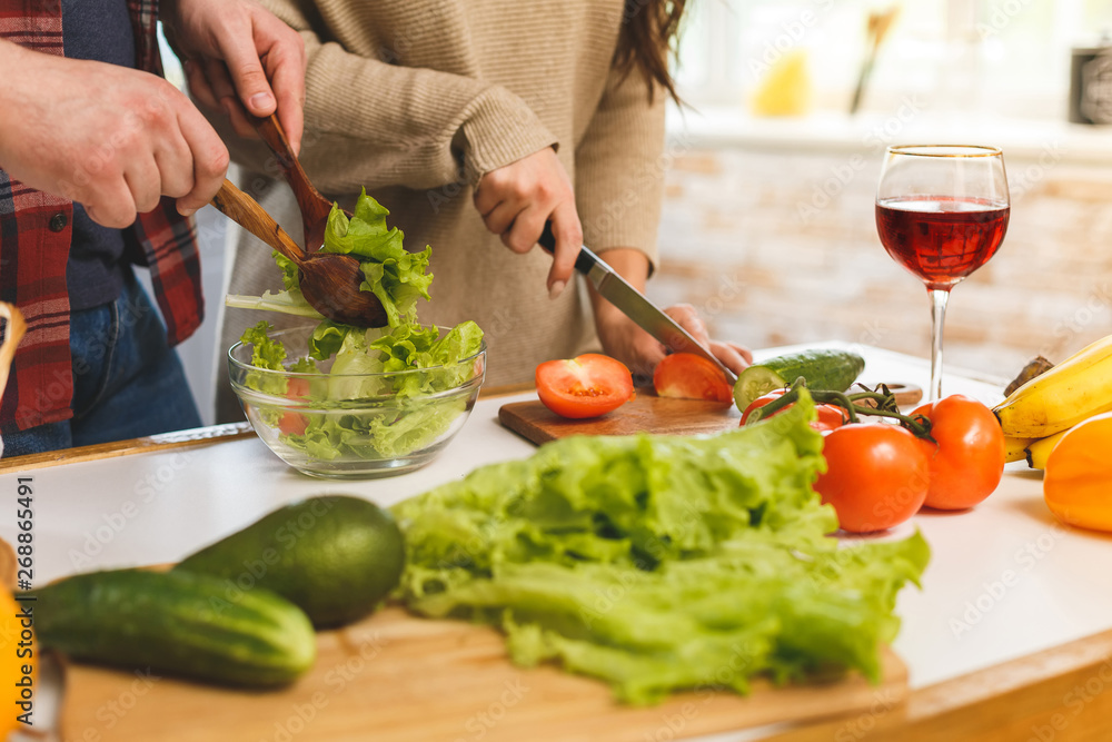 Beautiful young smiling happy couple is talking and smiling while cooking healthy food in kitchen at home. Close-up.