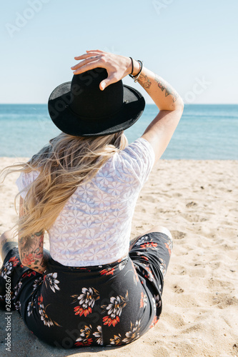 Blonde female sitting on a beach facing the water with her back to camera