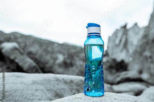 Aqua Blue Fitness Water Bottle Sitting Upon Rock with Mountains in Background. Environmental concept. Fitness concept. Health concept.