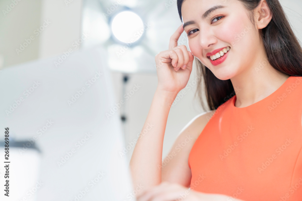 smart beautiful asian woman orange dress think smart and smiling hand finger touch head with laptop in office smart beautiful asian woman orange dress think smart and smiling hand finger touch head with laptop in office