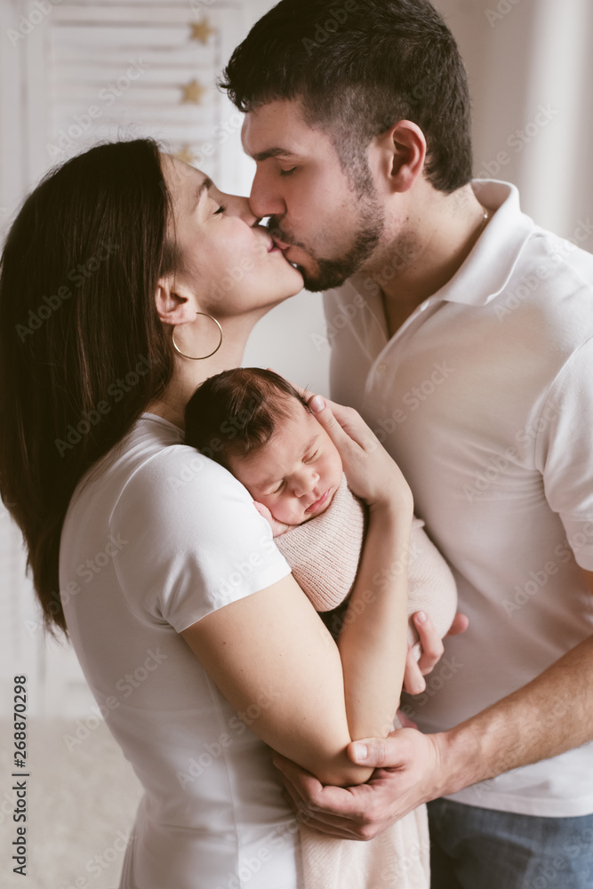 New mother and father holding their baby and kissing New mother and father holding their baby and kissing