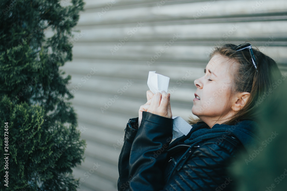 Young woman with brown hair wearing leather jacket and sunglasses sneezing in a white napkin with her eyes closed outdoor – Girl having an allergic reaction or a cold Young woman with brown hair wearing leather jacket and sunglasses sneezing in a white napkin with her eyes closed outdoor – Girl having an allergic reaction or a cold
