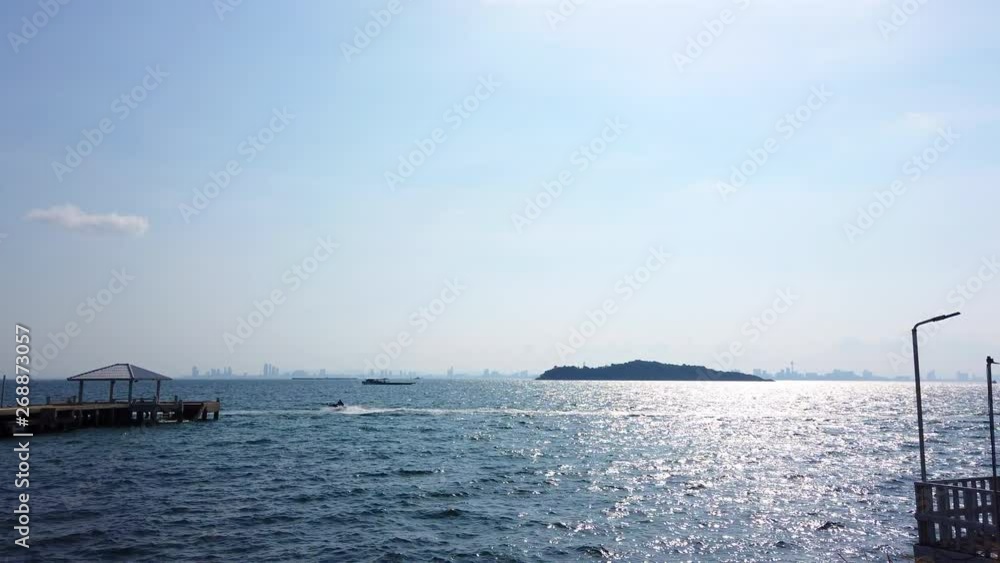 4K Video Selective focus landscape wide shot of moving sea water waves in the sea. The sun shining the sea surface with jet ski passing through the port and cityscape backgrounds in the morning. 4K Video Selective focus landscape wide shot of moving sea water waves in the sea. The sun shining the sea surface with jet ski passing through the port and cityscape backgrounds in the morning.