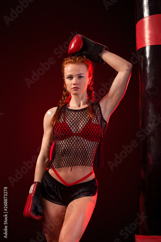 Young woman sportsman boxer doing boxing training at the gym. Girl wearing gloves, sportswear and hitting the punching bag. Isolated on black background with smoke. Copy Space.
