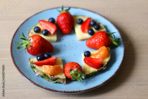 Various spring fruit on a turquoise plate: strawberries, pineapple, blueberries and tangerine. Selective focus.