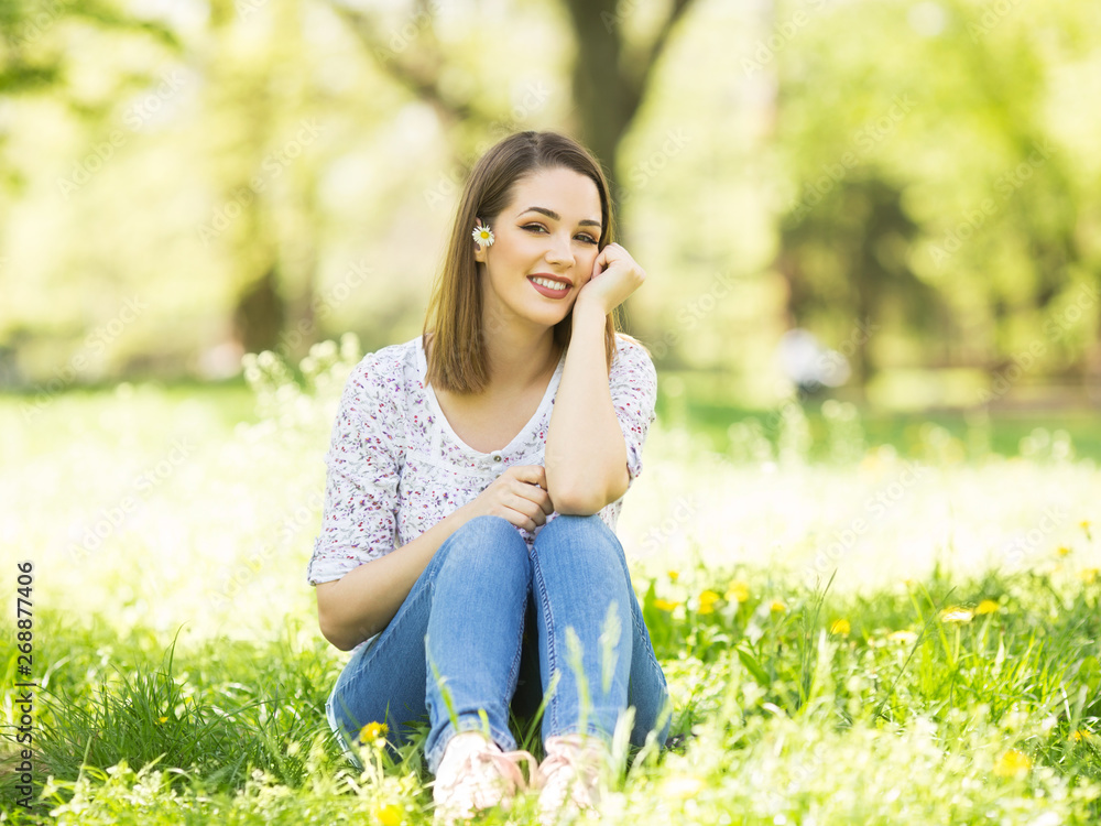 Beautiful young woman sitting in the grass and holding daisy flower Beautiful young woman sitting in the grass and holding daisy flower