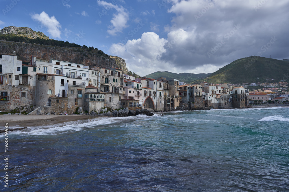 Cityscape Picture of old, ancient and romantic city Cefalu from seaside in italian island Sicily taken in sunny spring day with clouds on sky. Typical example of historic mediterranean architecture.