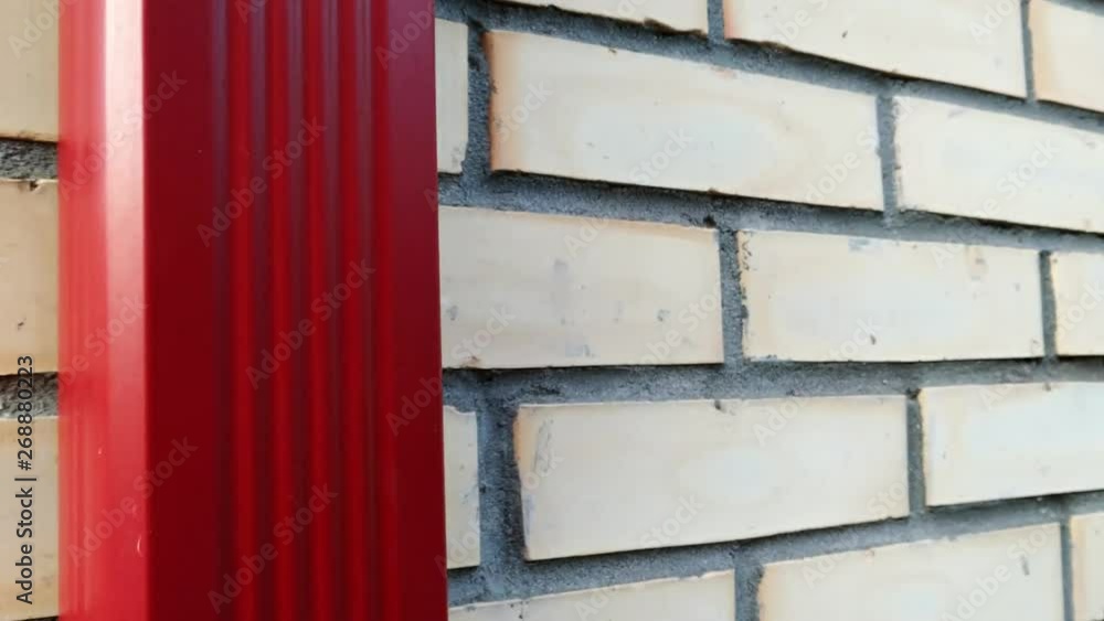Sliding down red metal rain gutter on white bricks wall. Sliding down red metal rain gutter on white bricks wall.