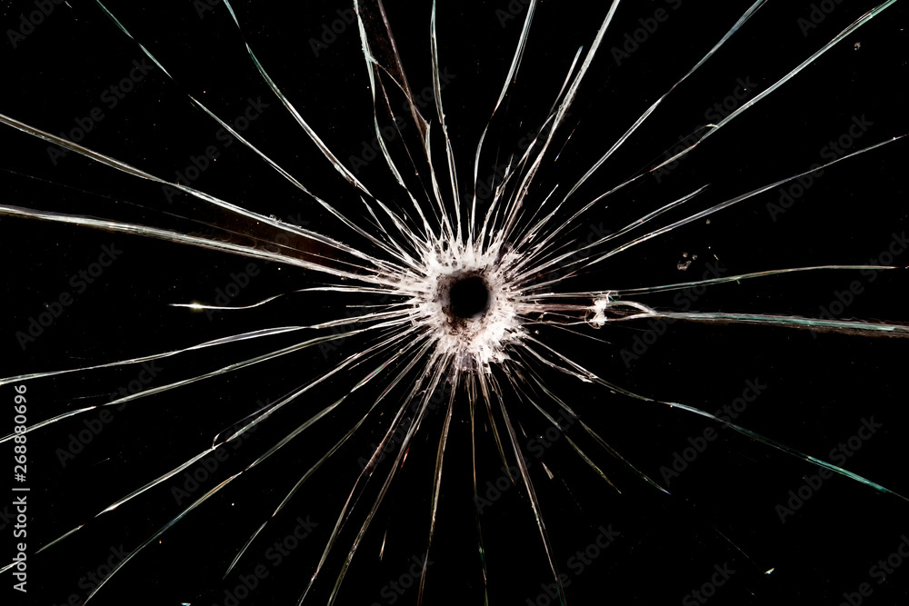 Obraz premium A bullet hole in glass. The background is black. Cracks radiate from the hole.