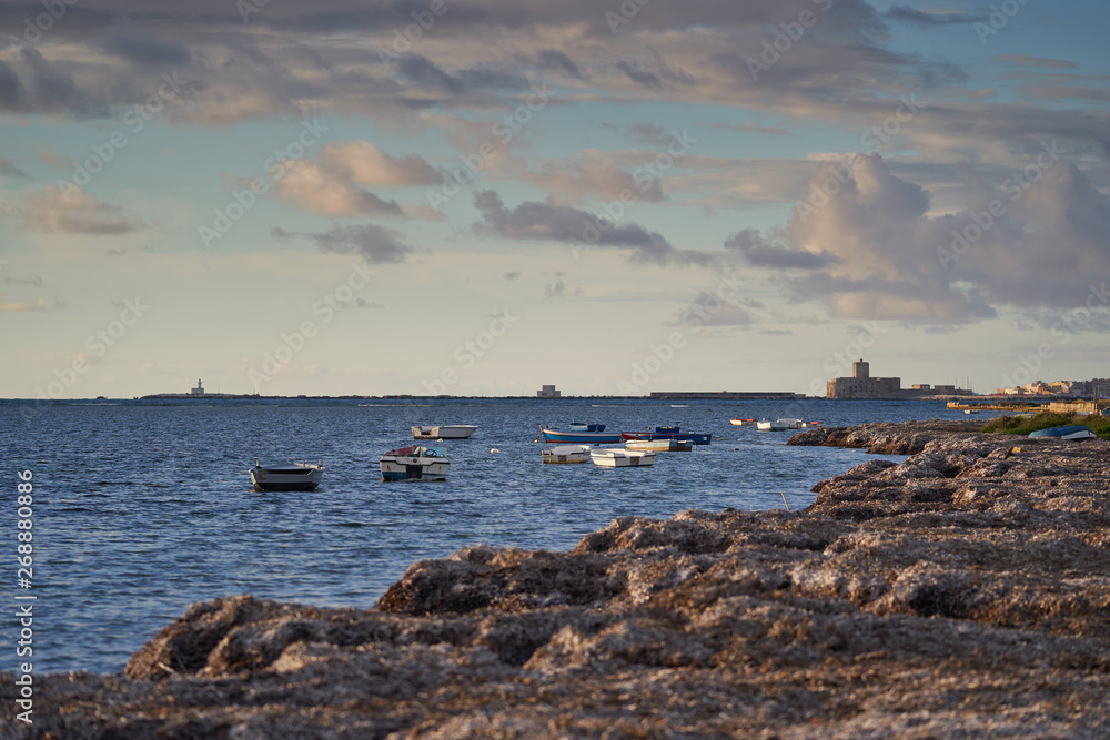 Landscape picture of the seaside or beach with rowboats and Trapani city with mediaeval fortress in background. Picture taken during summer sunset with cloudy sky in biggest italian island Sicily.