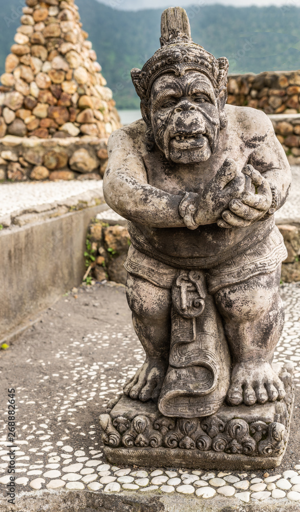 Bali, Indonesia - February 25, 2019: Ulun Danu Beratan Temple complex in Bedoegoel. Gray stone statue of dwarf in park. Bali, Indonesia - February 25, 2019: Ulun Danu Beratan Temple complex in Bedoegoel. Gray stone statue of dwarf in park.