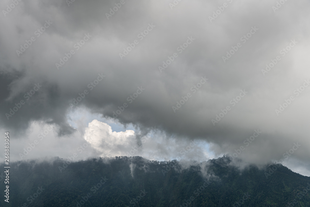 Bali, Indonesia - February 25, 2019: Rainy cloudscape over dark forested mountains in Bedougoel. Shades of gray.