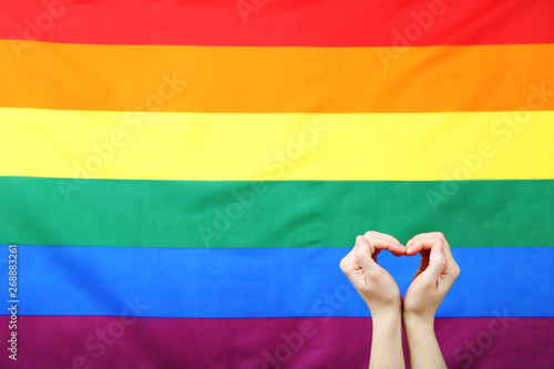 Female hands in shape of heart on rainbow flag background