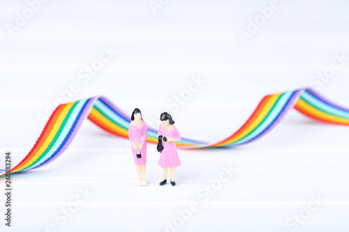 Miniature people with rainbow ribbon on white background