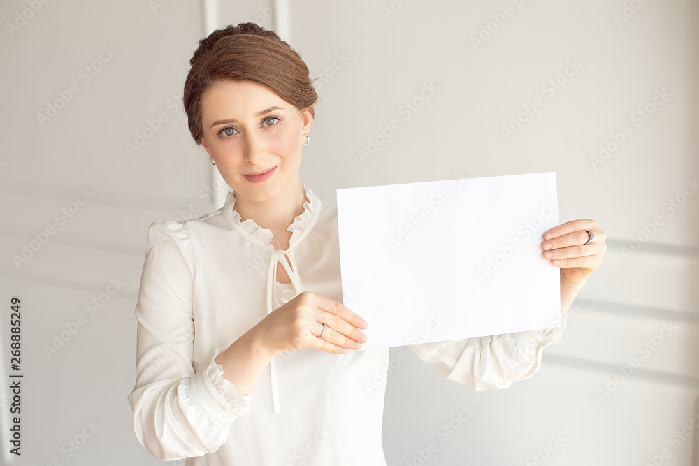 young smiling woman holding a blank sheet of paper for advertising.Girl showing banner with copy space. young smiling woman holding a blank sheet of paper for advertising.Girl showing banner with copy space.