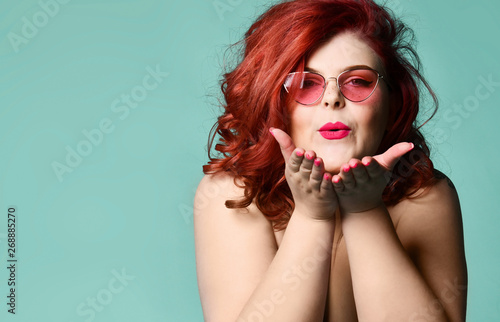 Plus-size overweight redhead lady in sunglasses send a kiss at free text copy space on mint photo