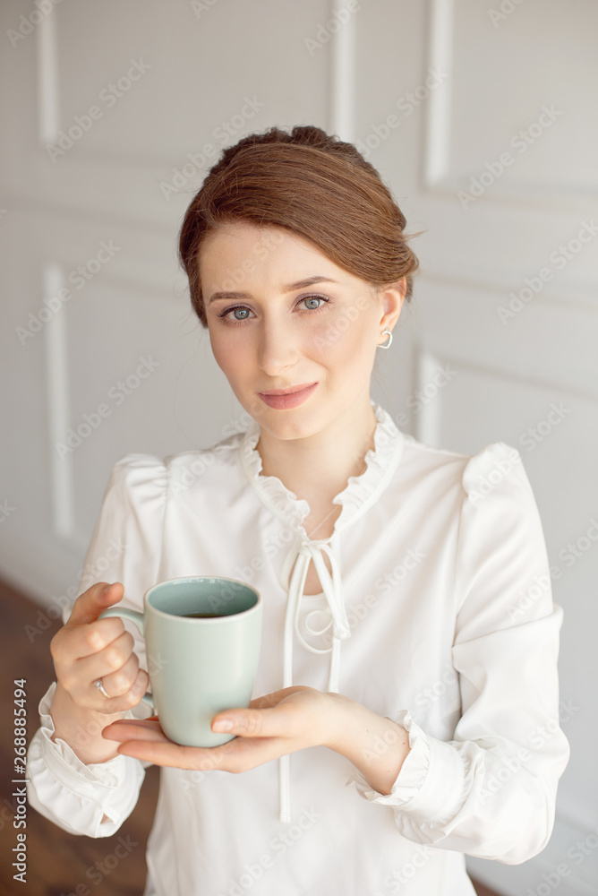 Attractive young woman in casual clothes is holding a cup, looking away and smiling, on white background Attractive young woman in casual clothes is holding a cup, looking away and smiling, on white background