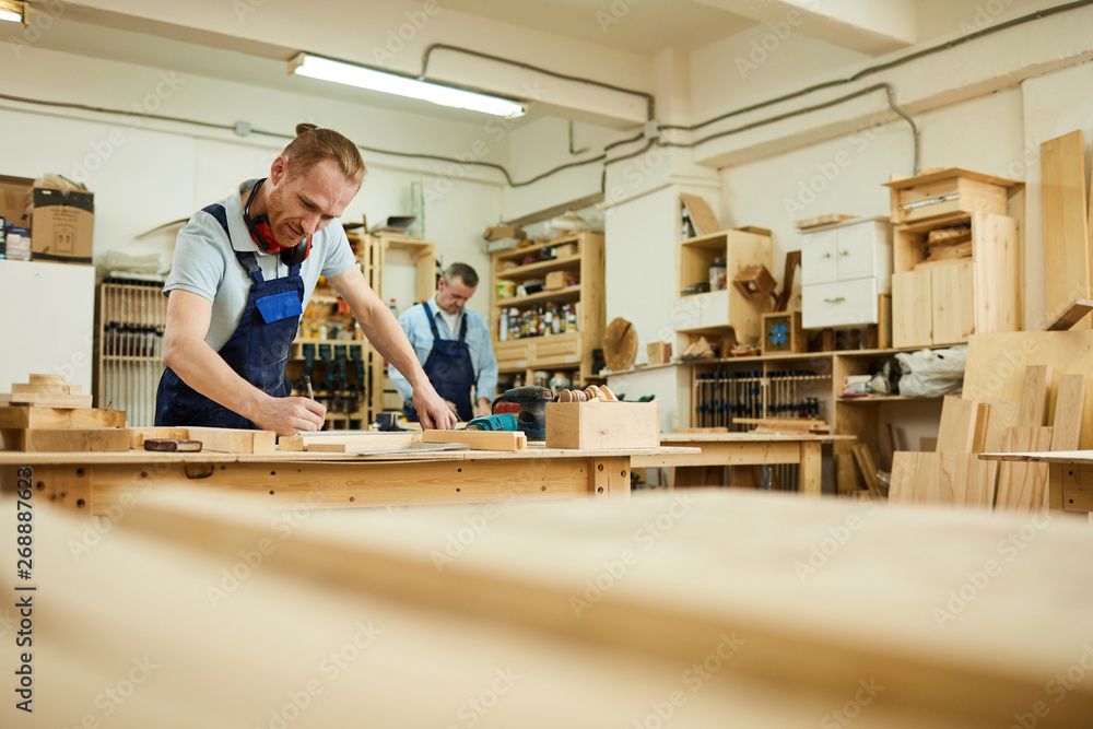 Wide angle portrait of two carpenters working with wood standing at tables in workshop, copy space