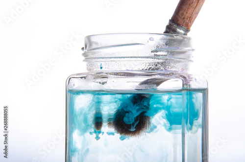 Paint brush in a can and a cloud of paint in water. White background. Blue