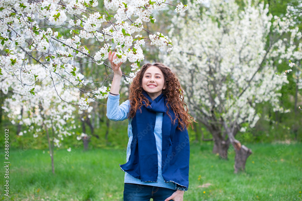 Portrait of a young beautiful fashionable woman in spring blossoming park. Happy girl posing in a blooming garden with white flowers Portrait of a young beautiful fashionable woman in spring blossoming park. Happy girl posing in a blooming garden with white flowers