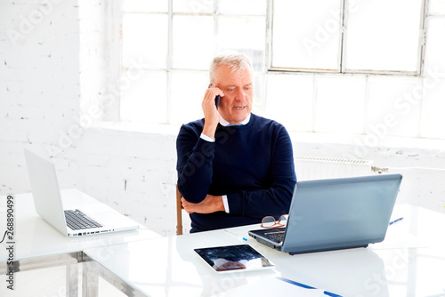 Senior businessman making a call while and using laptop while working in the office photo