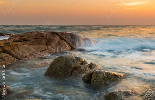 The rock and smooth sea wave in the sunset time.