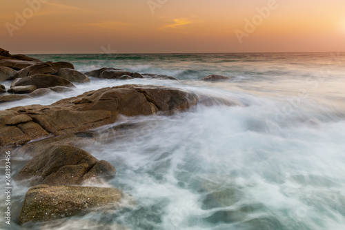 The rock and smooth sea wave in the sunset time.