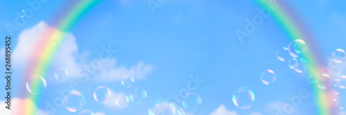  aufsteigende seifenblasen vor regenbogen am blauem himmel, sonniger hintergrund für sommer events,  konzept banner mit textraum photo