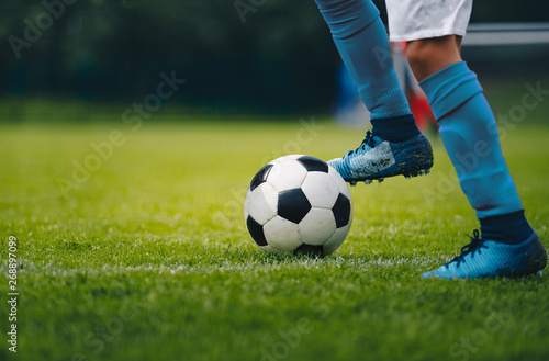 Fototapeta Naklejka Na Ścianę i Meble -  Close up of legs and feet of football player in blue socks and shoes running and dribbling with the ball. Soccer player running after the ball. Sports venue in the background