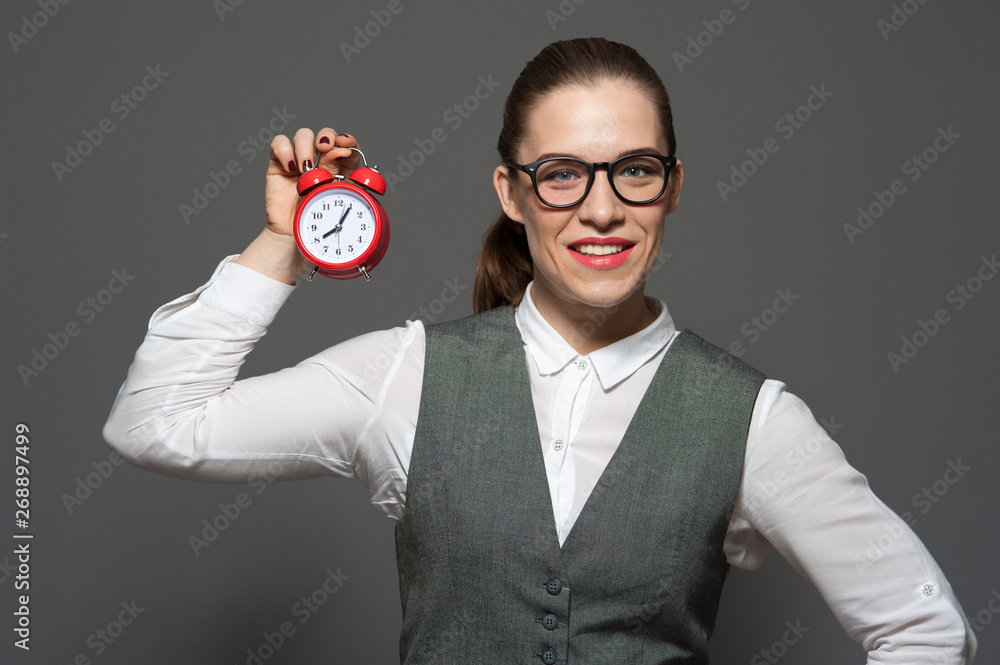 Charming businesswoman or office worker in formal suit holding red clock Charming businesswoman or office worker in formal suit holding red clock