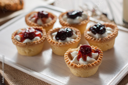 Delicious homemade mini berry tarts and custard on wooden cutting board