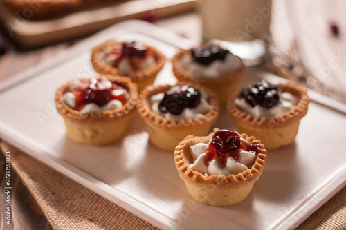 Delicious homemade mini berry tarts and custard on wooden cutting board