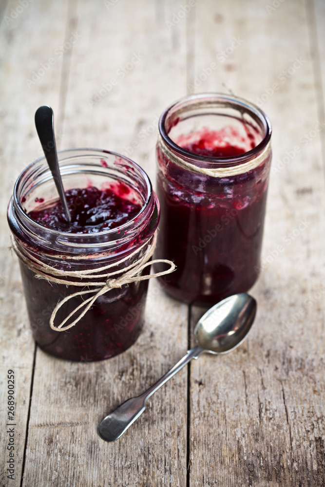 Two jars of fresh cherry and wild berries  homemade jam in jar on rustic wooden background.