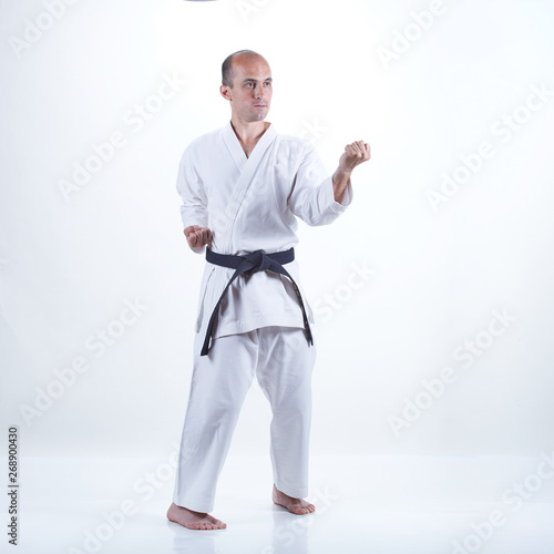 Young athlete with black belt trains formal karate exercises on a light background