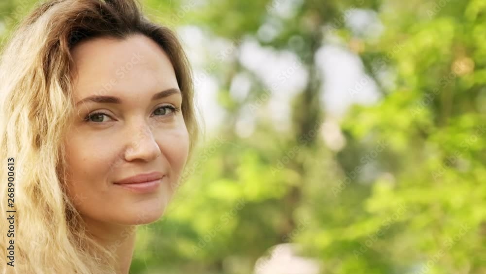 Beautiful adult woman on the nature. adult girl posing in the park. Happiness concept. Outdoors portrait of a blonde woman with long curly hair in the park. Smiling female face. Slow motion. Beautiful adult woman on the nature. adult girl posing in the park. Happiness concept. Outdoors portrait of a blonde woman with long curly hair in the park. Smiling female face. Slow motion.