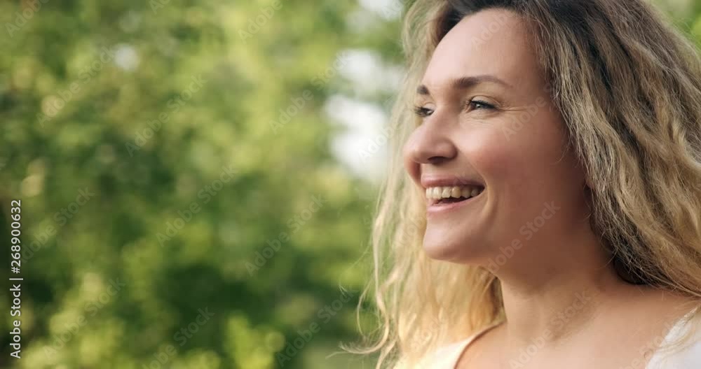 Adult woman blowing on the dandelions on the nature. Happy adult girl blows dandelions. Happiness concept. Outdoors portrait of a blonde woman with long curly hair in the park. Smiling female face Adult woman blowing on the dandelions on the nature. Happy adult girl blows dandelions. Happiness concept. Outdoors portrait of a blonde woman with long curly hair in the park. Smiling female face