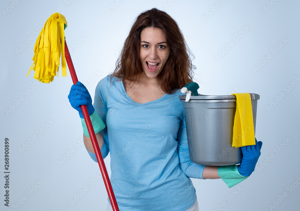 Young attractive woman holding cleaning tools and products in bucket isolated on blue background Young attractive woman holding cleaning tools and products in bucket isolated on blue background