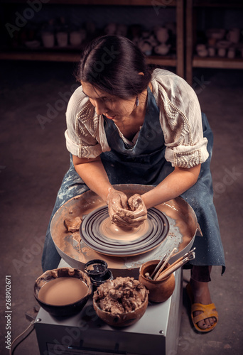 Charming artisan girl sculptor works with clay on a Potter's wheel and at the table with the tools. Handicraft industry. photo